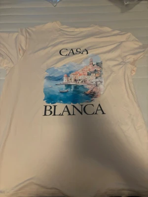 Beige Casa Blanca t-shirt med tryck - Snygg beige t-shirt från Casa Blanca med färgglatt tryck av en kuststad och texten 'Casa Blanca' både fram och bak. Helt ny.