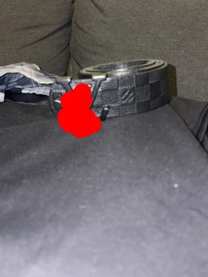 Svart rutigt skärp med metallspänne - Säljer ett svart skärp med rutigt mönster och stilrent metallspänne. Skärpet har en modern look och är tillverkat i skinn, perfekt för att lyfta din outfit. Passar dig som gillar accessoarer med diskret men cool design. Utsidan är i bra skick men insidan ser man den är använd. Storlek 115/46