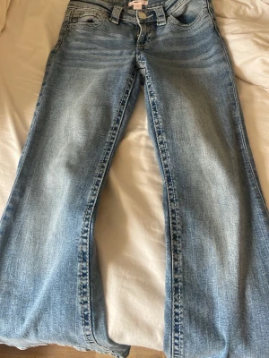 Ljusblå bootcut jeans från Gina Tricot - Säljer ett par ljusblå bootcut jeans från Gina Tricot med klassisk femficksmodell och snygg tvätt. Jeansen har hög midja, dragkedja och knapp framtill samt breda benslut för en trendig look.