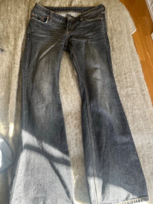 Bootcut jeans i mörkblå denim - Säljer ett par snygga bootcut jeans i mörkblå denim med klassiska fem fickor och orangea sömmar. Jeansen har låg midja och utsvängda ben, perfekta för en avslappnad och trendig look. Passar dig som gillar retrovibbar och tidlös stil.