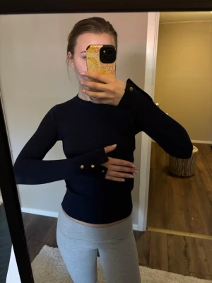 Marinblå långärmad topp med knappar - Säljer en marinblå långärmad topp med tight passform och dekorativa knappar vid ärmsluten. I storlek xs köp från Lindex💕🤗.