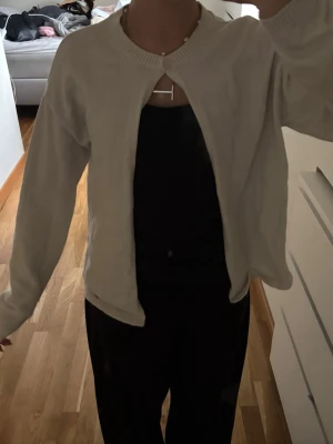 Kräm vit stickad kofta - Säljer en beige stickad kofta med lång ärm en knapp som knäppning framtill. Koftan har rund halsringning och ribbade muddar vid ärmslut och nederkant. Perfekt att slänga över en topp för en enkel men snygg look.