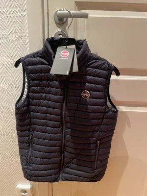 Svart dunväst från Colmar - Snygg svart dunväst från Colmar med quiltad design och hög krage. Västen har dragkedja framtill, den säljs på grund av att den inte längre kommer till användning, priset kan alltid ändras vid en snabbaffär. 