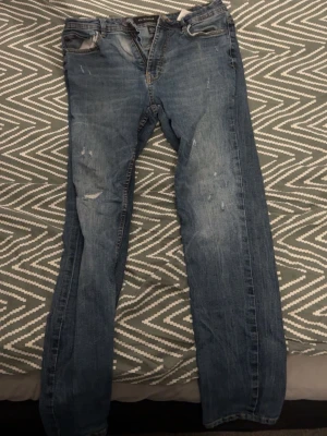 Blå raka jeans  - Säljer ett par blå jeans från Jack & Jones med rak passform och lätt slitna detaljer. Jeansen har klassisk femficksdesign och är tillverkade i denim. Perfekta för en avslappnad stil.