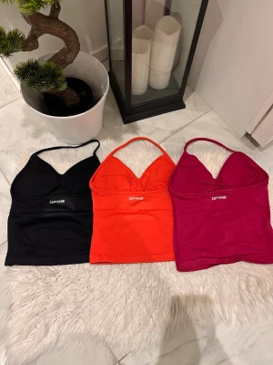 DFYNE croppade linne-toppar - Tre croppade linne-toppar från DFYNE i svart, röd och rosa. Topparna har smala axelband, lätt v-ringad byst och logga framtill. Perfekta för en trendig och sportig look. Materialet är stretchigt och mjukt, troligen polyester eller syntet. MODELL: impact. Midnight black , chili och den sista finns inte på hemsidan längre 