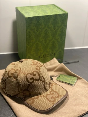 Gucci keps  - Säljer en beige keps från Gucci med det klassiska GG-monogrammet i brunt över hela kepsen. Kepsen har böjd skärm och bruna detaljer längs kanterna. Tillverkad i canvasmaterial