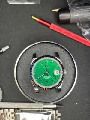 Seiko klocka med grön urtavla - Snygg Seiko klocka med grön urtavla och arabiska siffror. Boetten och länken är i silverfärgat metall och klockan har en räfflad bezel samt datumfönster med förstoringsglas. Perfekt för dig som vill sticka ut med en unik accessoar.