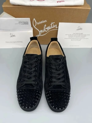 Louboutin skor  - Säljer ett par svarta sneakers från Christian Louboutin i mocka med svarta nitar på tån. Skorna har klassisk låg profil, svarta skosnören och en stilren design som sticker ut. Perfekta för dig som vill ha något extra till din outfit.