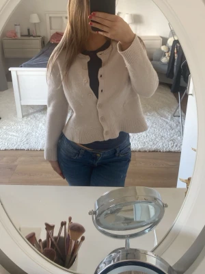 Kofta med knappar - Söt krämvit kofta med rund hals och ribbade muddar. Koftan har långa ärmar och stängs med matchande knappar framtill. Använd några gånger men är i bra skick!🥰