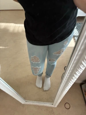 Ljusblå ripped jeans med hål - Säljer ett par ljusblå jeans med flera stora slitningar och hål framtill på benen. Jeansen har en smal passform och klassisk femficksdesign. Perfekta för dig som gillar en avslappnad och trendig stil.