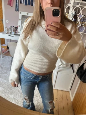 Vit croppad stickad tröja - Säljer en vit croppad stickad tröja med breda ärmar och ribbad midja. Tröjan har en enkel och stilren design som passar perfekt till jeans eller kjol. Materialet känns mjukt och bekvämt mot huden.