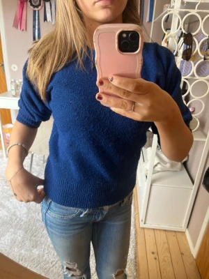 Kornblå stickad tröja med puffärm - Snygg kornblå stickad tröja med korta puffärmar och ribbstickade muddar. Tröjan har en klassisk rund halsringning och är perfekt att matcha med jeans. Materialet känns mjukt och bekvämt mot huden.