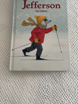 Jefferson tar täten bok - En skönlitterär bok med hård pärm, illustrerat omslag där en djurkaraktär åker skidor i vinterkläder. Boken är utgiven av Lilla Piratförlaget och har en vintrig, fantasifull känsla. Perfekt för dig som gillar äventyr och djur i berättelser.