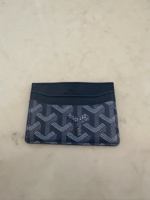 Mörkblå korthållare - Snygg mörkblå korthållare från  med det klassiska vita och gråa mönstret. Tillverkad i Frankrike och gjord i läder med flera fack för kort. Perfekt accessoar för dig som gillar exklusiva detaljer.