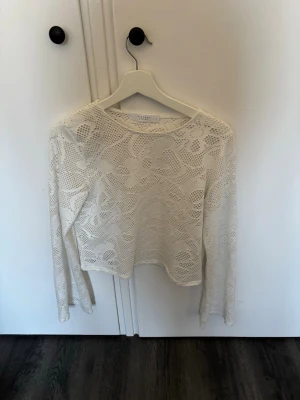 Vit spetsblus från Sisters Point - Säljer en superfin vit långärmad blus från Sisters Point. Blusen är helt i spets med blommigt mönster och har en croppad passform. Perfekt att styla med ett linne under för en trendig look.