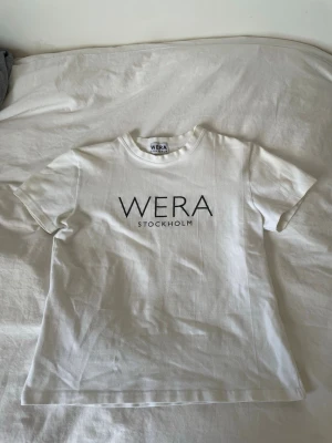 Vit t-shirt från Wera Stockholm - Vit t-shirt från Wera Stockholm med svart tryck framtill. Klassisk rund halsringning och korta ärmar. Perfekt till en basic outfit! Stor ej storlek i den men är typ en S 