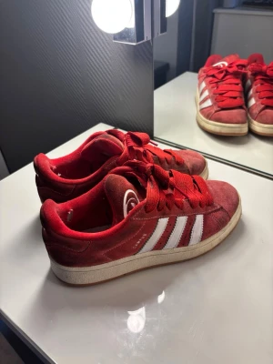Röda Adidas Campus - Snygga röda Adidas Campus i storlek 39 1/3. Skorna är använda och har små hål på insidan vid hälen (se sista bild) annars fungerar dem fin fint!🌟