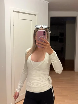 Vit omlottopp från MILK - Säljer en vit tränings omlottopp från Nelly med långa ärmar och knytband i sidan. 