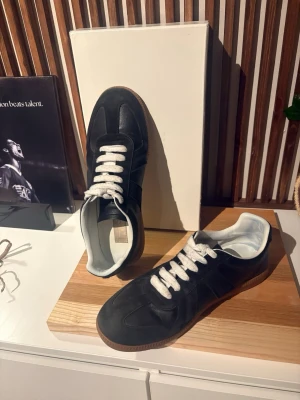 Mason Margiela Gats - Upptäck den perfekta kombinationen av stil och komfort med dessa exklusiva svarta sneakers. Tillverkade med omsorg och uppmärksamhet på detaljer, är dessa skor ett måste för alla modeintresserade. Den eleganta svarta designen passar perfekt till alla outfits, från avslappnade jeans till mer dressade byxor. Den högkvalitativa konstruktionen säkerställer både hållbarhet och en oslagbar känsla. Det ända lilla slitage är på sulan under skon!