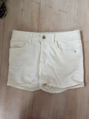Vita höga shorts i bomull - Snygga vita shorts med hög midja och klassisk femficksdesign. Gjorda i mjuk bomull med knapp och dragkedja framtill. Perfekta till sommaren och lätta att matcha med olika toppar.