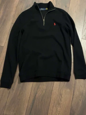 Svart Ralph lauren halv zip M - Svart långärmad tröja från Polo Ralph Lauren med halvzip och ståkrage. Tröjan har det klassiska röda broderade logot på bröstet och är tillverkad i mjukt material. Perfekt för en stilren och avslappnad look.