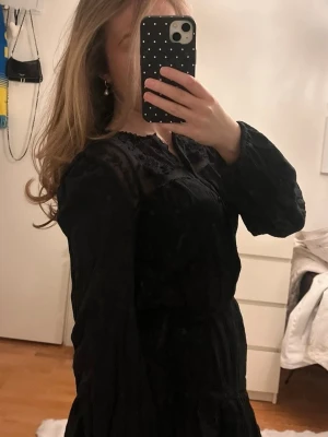 Svart kort klänning med spetsdetaljer - Säljer en svart kort klänning med långa ärmar och spetsdetaljer upptill. Aldrig använd pga lite stor. 