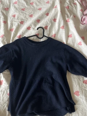 Mörkblå stickad tröja med midja - En enkel och stilren mörkblå stickad tröja med rund halsringning och ribbade muddar. Tröjan har en rak passform med en ribbad midja och är perfekt för lager-på-lager. Materialet ser mjukt och lite luddigt ut, vilket ger en mysig känsla.