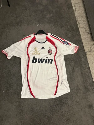 AC Milan bortatröja Maldini #3 Adidas - Säljer en vit AC Milan bortatröja från Adidas med röda detaljer och svarta inslag.  Tröjan har trycket 'Maldini' och nummer 3 på ryggen, Champions League-märke på ärmen och Bwin som sponsor på bröstet. Perfekt för fotbollsfans och samlare.