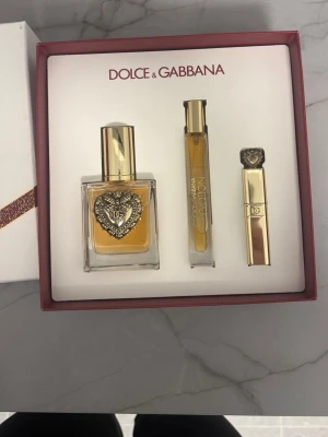 Dolce & Gabbana Devotion presentset - Lyxigt presentset från Dolce & Gabbana med Devotion Eau de Parfum 50 ml, en 10 ml parfymflaska och en guldig mascara. Flakongen har ett elegant hjärtdetalj i metall och guldfärgade lock. Perfekt för dig som gillar exklusiva dofter och snygg design.