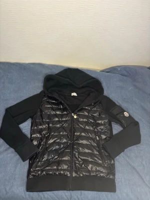 Svart moncler cardigan - Snygg svart pufferjacka från Moncler med glansig quiltad framsida, huva och dragkedja. Jackan har Moncler-logga på ärmen och den går även att skanna med mobilen.