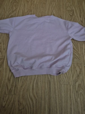 Ljuslila sweatshirt utan huva - En basic ljuslila sweatshirt i mjukt material med rund halsringning och ribbade muddar vid ärmslut och nederkant. Perfekt för en avslappnad och stilren look. Ingen synlig logga eller märke på tröjan.