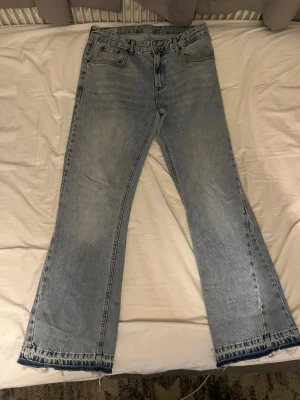 Ljusblå bootcut jeans från Zara - Säljer ett par ljusblå bootcut jeans från Zara med klassisk femficksdesign och råa kanter nertill. Jeansen har en avslappnad passform och är tillverkade i bomullsdenim. Perfekta för en trendig och avslappnad stil.