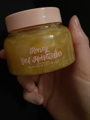 Honey Gel Moisturiser ansiktsgel - Säljer en Honey Gel Moisturiser i en genomskinlig burk med ljusrosa lock. Gelen har en gyllene, skimrande färg och är perfekt för att återfukta huden. Innehåller 120 g och har en söt design med text i rosa. Endast använd några gånger!
