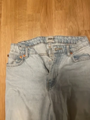 Ljusblå jeans från 157 - Säljer ett par ljusblå jeans från 157 med klassisk femficksdesign och raka ben. Jeansen har en avslappnad passform och är tillverkade i bomull. Perfekta för en casual och trendig look.