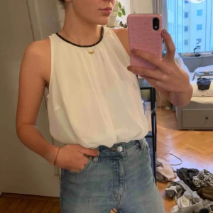  - Vit topp i chiffong med en kant i svart skinnimitation kring halsen. Priset är exklusive frakt. 