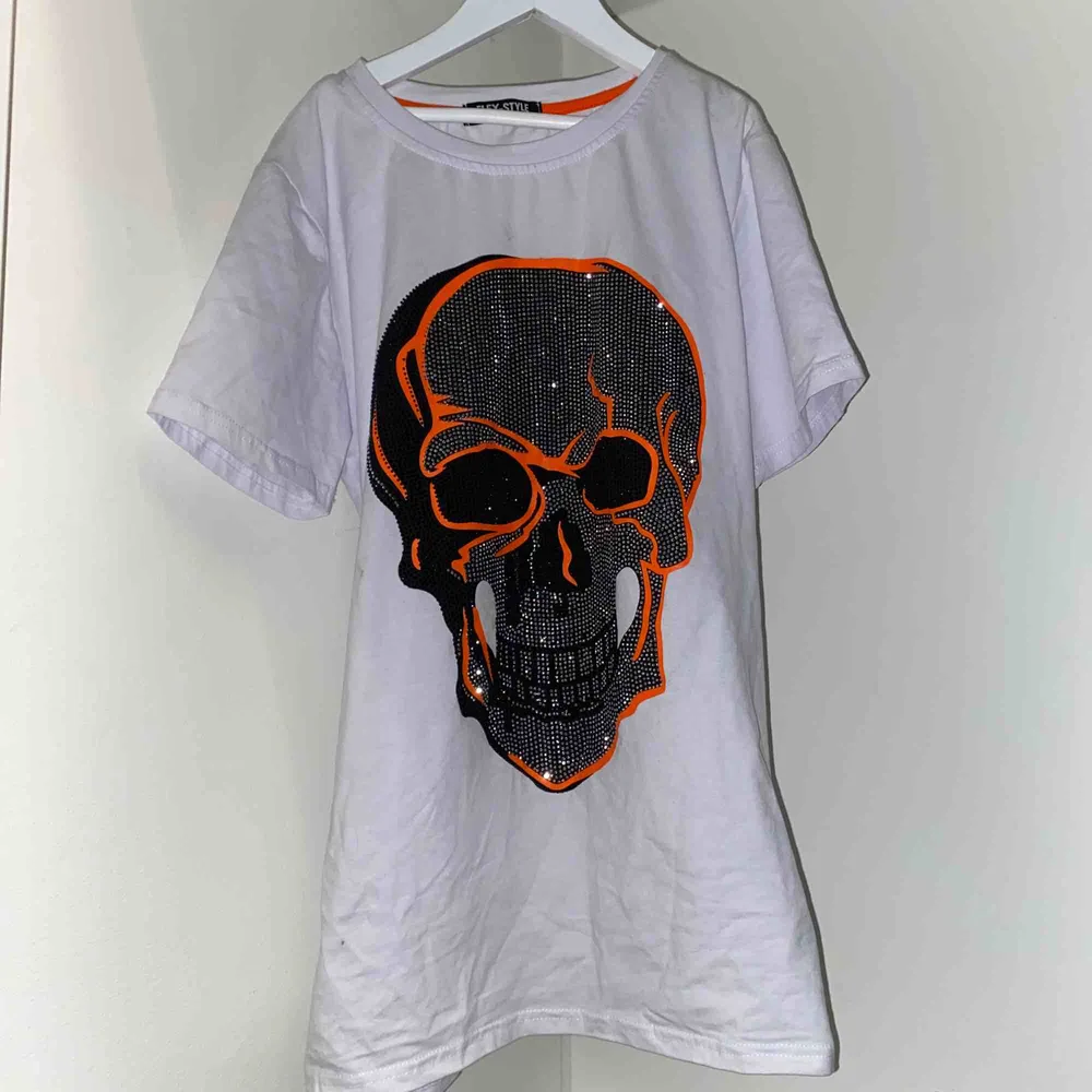 En vit T shirt med en svart döskalle som har silvriga paljetter. Dödskallen har oranga kontraster. Har används 1 gång.. T-shirts.