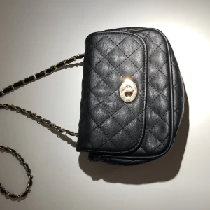 Väska - Svart väska av fejkläder. Guldaccessoar till spänne. Användes inte längre. I bra skick. Frakt tillkommer.