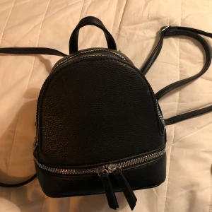 Mini ryggsäck - Miniryggsäck i fake skinn. 2 fack med dragkedja. Sjusterbar axelrämmar