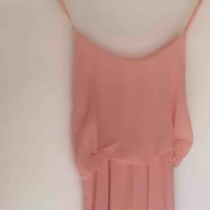  - Rosa Långklänning 💖 Använd på ett bröllop. Smala axelband och skirt tyg. Använde säkerhetsnålar för att ”knyta in” tyget i midjan (bild 1). Utan nålarna hänger tyget mer fritt (bild 2).  Graciös klänning i fint skick.