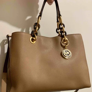  - Sparsamt använd Michael Kors väska i läder från 2016. Ljus brun/beige färg. Gulddetaljer, handtag och axelrem.  Knappt använt denna väska, endast fåtal gånger så skicket är väldigt bra. Förvaringspåse kommer med.  Nypris var 3500. Inga skambud tack :)  