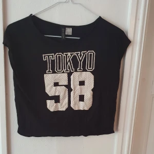 Svart croptop med tryck - Svart croptop med trycket "Tokyo 58" i vitt. Storlek XS men lite oversize ⭐ Köpt på H&M för några år sedan men har inte blivit använd på länge och sälher därför ⭐ Fortfarande i bra skick! Kontakta vid frågor/intresse 💜 frakt inräknad