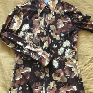 Skjorta 70-tal  - Skjorta i stretchig polyester från 70-talet, storlek small/36-38. Färgerna är aningen varmare än vad som syns på bilderna. Köpt i London men aldrig använd av mig. Mått tvärs över från armhåla till armhåla 43 cm, längd 59 cm. Köparen betalar frakten