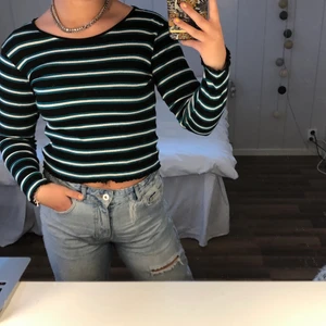 Randig Tröja Från Gina Tricot - Superfin långärmad tshirt från Gina Tricot som jag köpte för ca 2år sedan. Den är använd några få gånger men är i nyskick! Tröjan är svart med vita och gröna ränder samt har ”volanger” i sömmen längst ut på ärmen och nertill. 