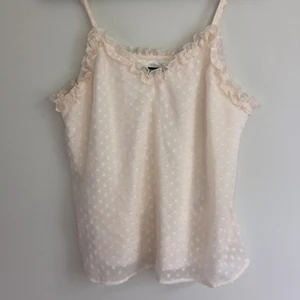 Bikbok linne stl xs  - Aldrig använd! Jättegulligt linne från bikbok i vit/beige. Prickigt med lite glitter och volanger längs med överkanten. Köparen står för frakten. 