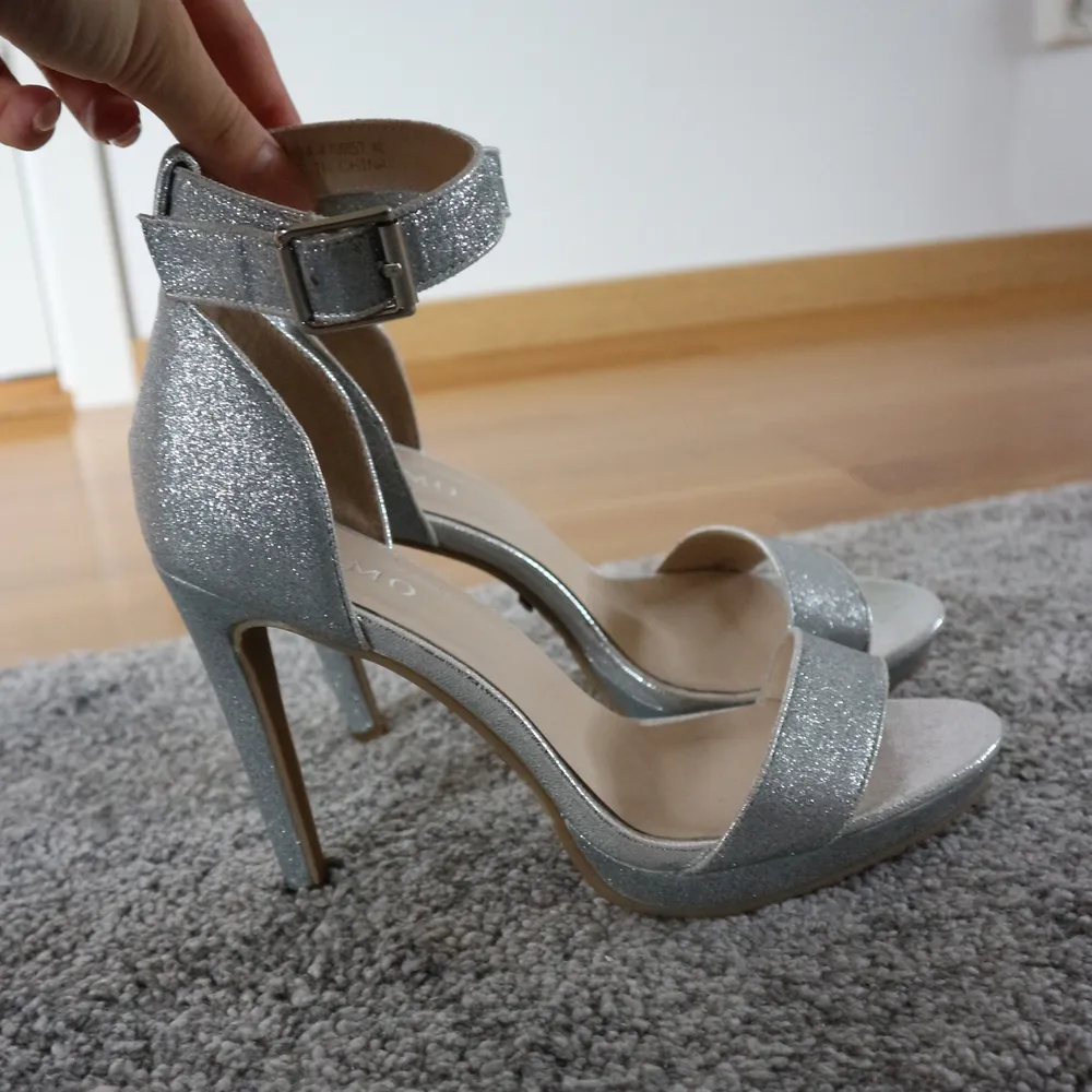 Säljer ett par väldigt snygga och festliga sandaler som är silver glittriga. Klackarna har en 11cm lång klack och är i storlek 40. De är från Tiamo och har endast burits en gång.. Kengät.