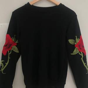 En vanlogt svart sweatshirt med ros detaljer på ärmarna. 