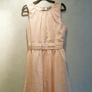Ljusrosa, kort dressad klänning - Jättefin klänning som är använd 2 gånger. Har en tight passform och har underklänning i silkigt tyg som sitter åt lite mer. Yttre tyget är tunt och luftigt. Något öppen i rygg (ett kortare sprund) som stängs i nacken med knapp samt gömd dragkedja i sidan.