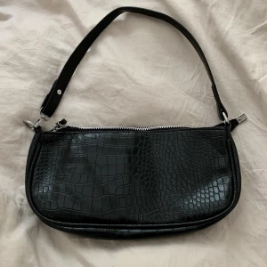 Baguette bag - Väska från Le Balina store. Nypris 350kr. Väskan är oanvänd. Kom med prisförslag men inte lägre än 100kr. Frakt på 60kr tillkommer.  Storlek: 29 cm x 13,5 cm  Updelning i 2 innerfickor för att passa i smartphones, nycklar och kort.  100% vegan - Krokodilmönstereffekt och PU-material. LEDANDE BUD: 160kr. Budgivningen avslutas på söndag. 