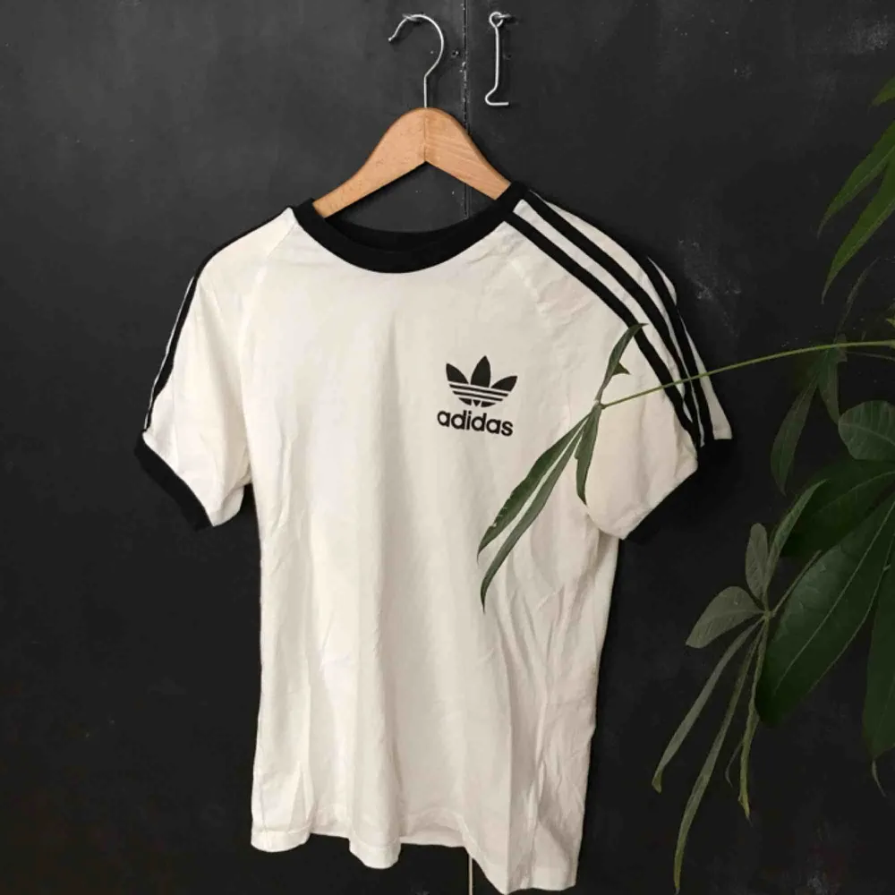 Felfri t-shirt från Adidas som helt enkelt inte används längre! Syns inte helt med bakgrunden men svarta muddar i ärmar och ringning, samt klassiska ränderna längs ärmarna!. T-shirts.