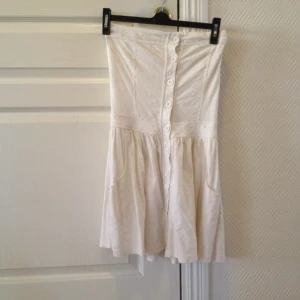 Vit klänning med små blommiga broderier och knappar.  - Vit klänning med små blommiga broderier och knappar. 